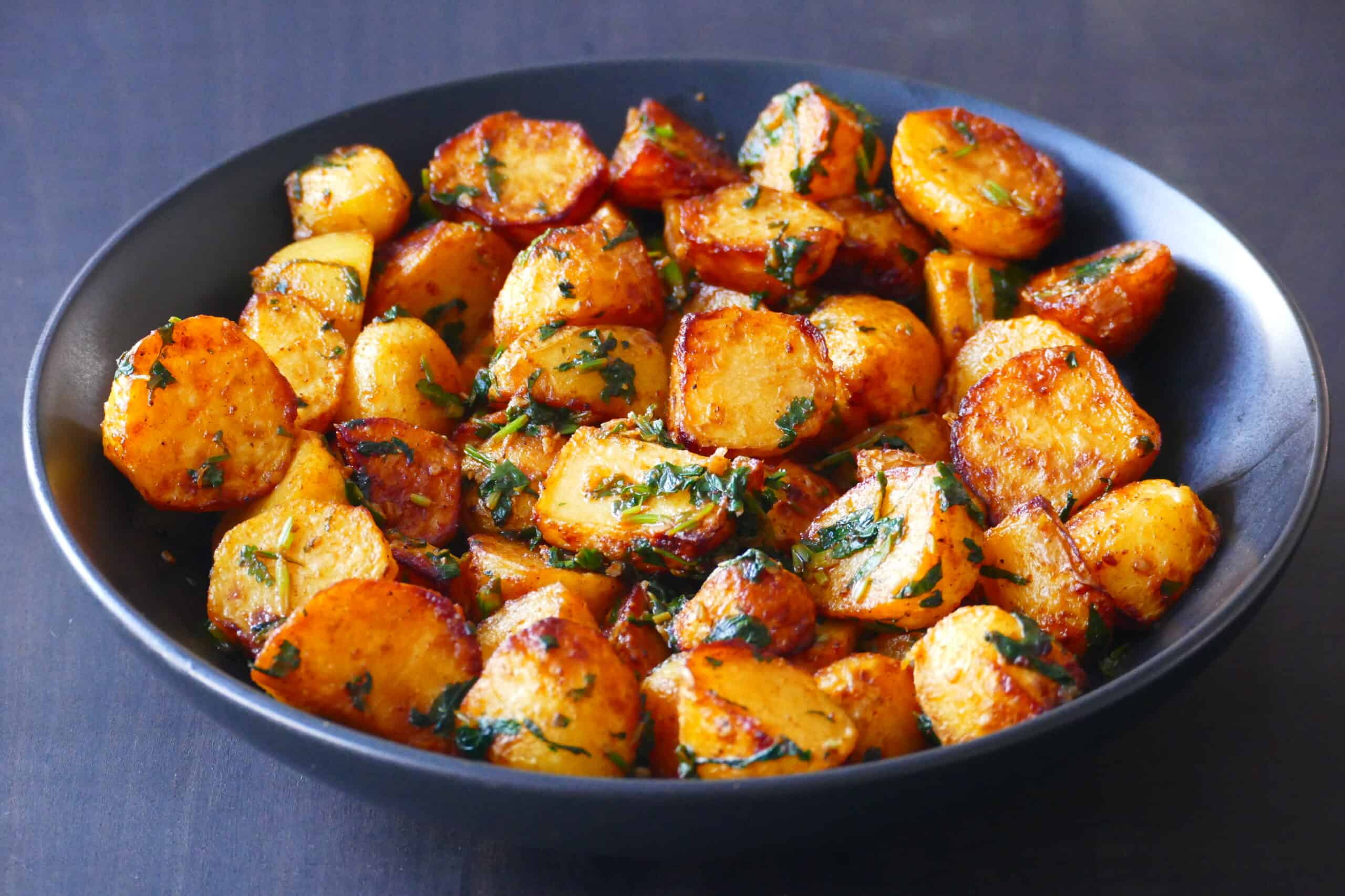 Black bowl with golden roasted potatoes coated with cilantro sauce