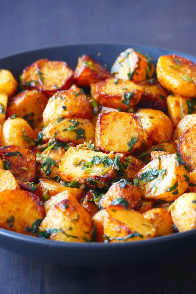 Black bowl with golden roasted potatoes coated with cilantro sauce