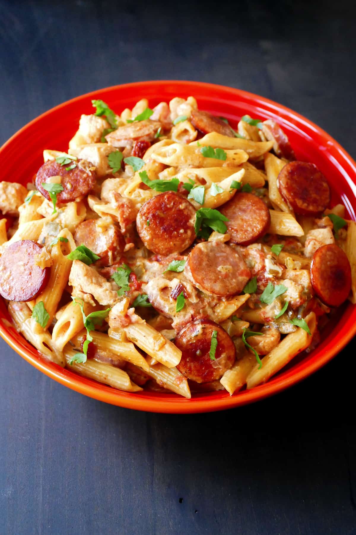 Instant Pot Cajun chicken pasta in red bowl with pasta, sausage, chicken, garnished with parsley.