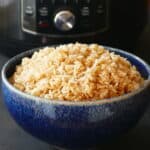 Heaping mound of brown rice in a blue bowl in front of a black Instant Pot.