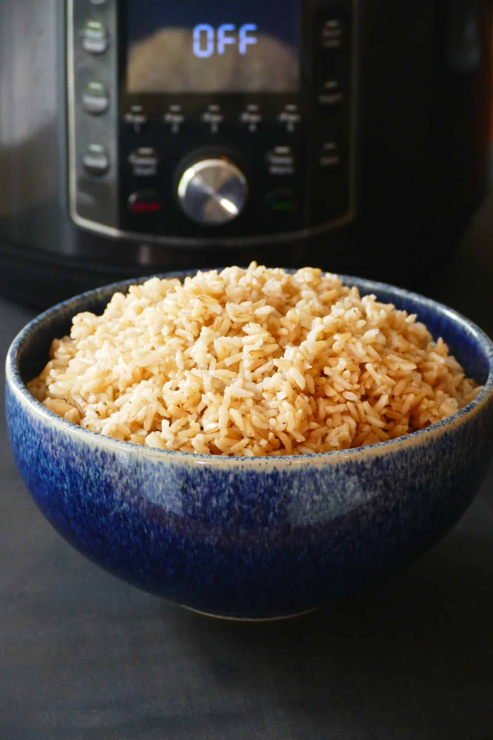 Heaping mound of brown rice in a blue bowl in front of a black Instant Pot.