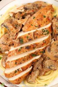 sliced chicken with mushrooms and sauce on a bed of pasta
