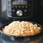 Instant Pot Jasmine Rice - A heaping mound of brown rice in a blue bowl in front of a black instant pot.