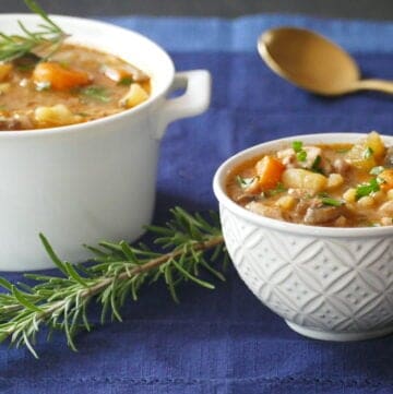 Serving bowl and small bowl with chicken stew with potatoes, carrots, parsley and spring of rosemary.