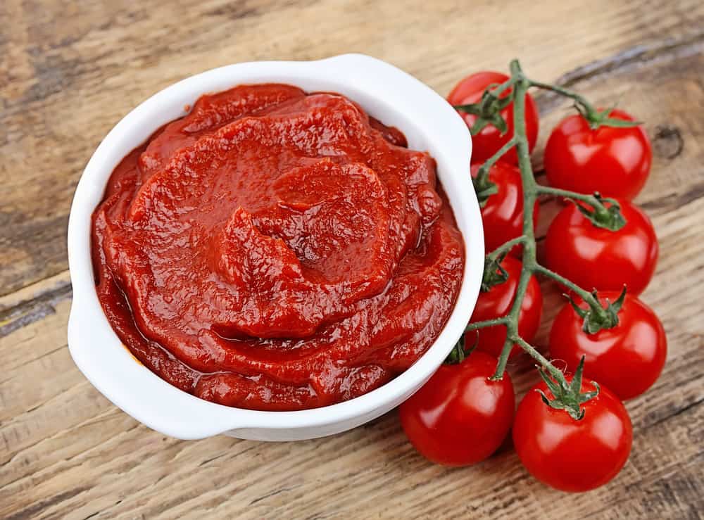 White bowl with tomato sauce and ripe tomatoes on wooden background.