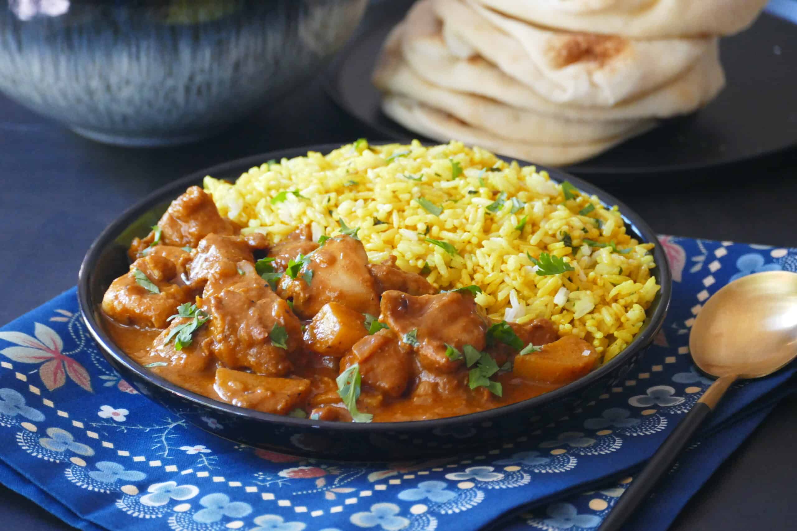 butter chicken and yellow rice with naan in background.