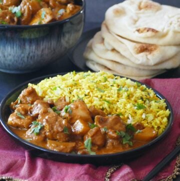 Kerala chicken curry with yellow rice in a black plate with naan stacked in background.