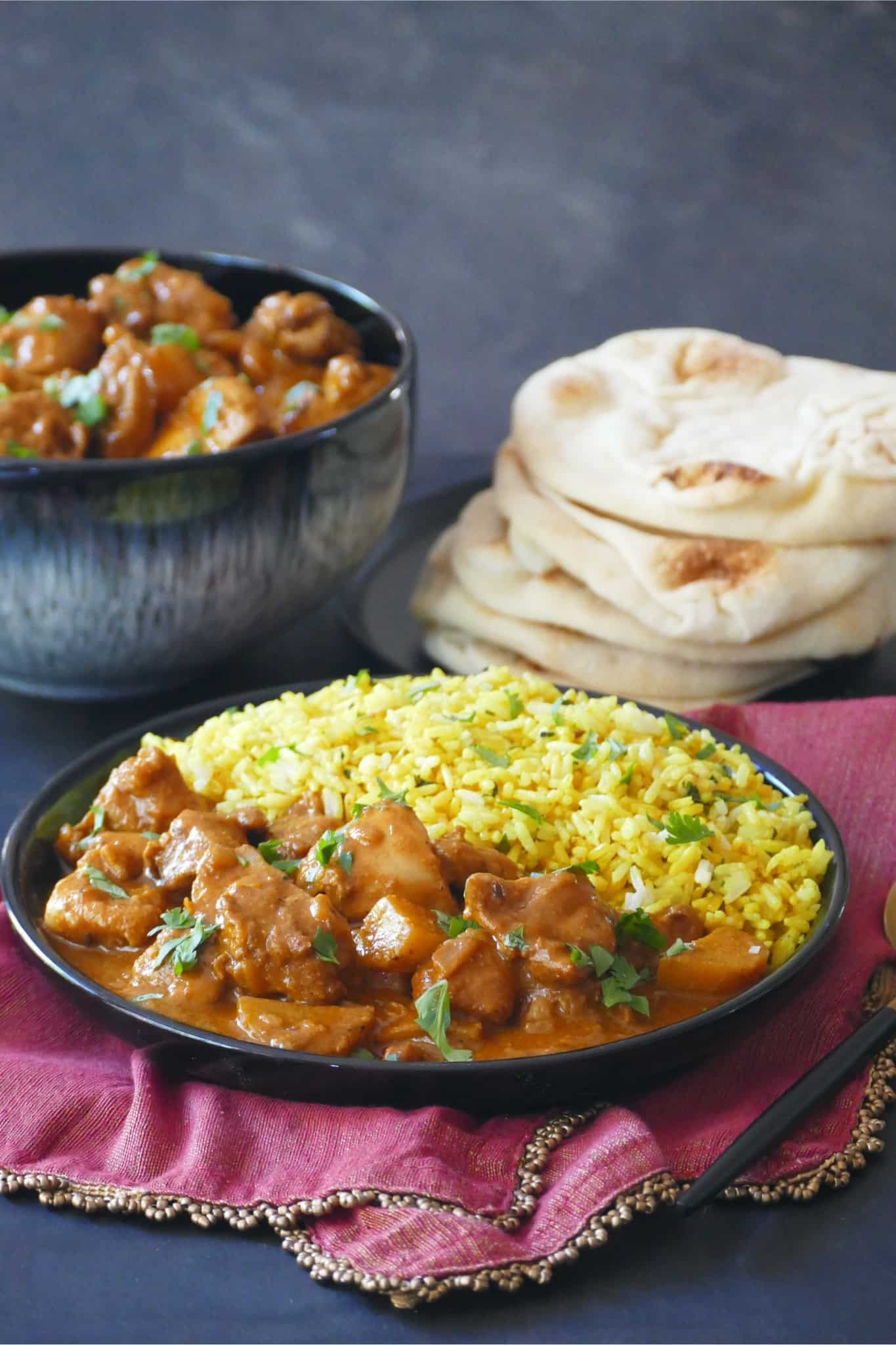 Kerala chicken curry with yellow rice in a black plate with naan stacked in background.