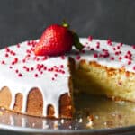 Frosted air fryer pound cake with a strawberry on top on metal tray.