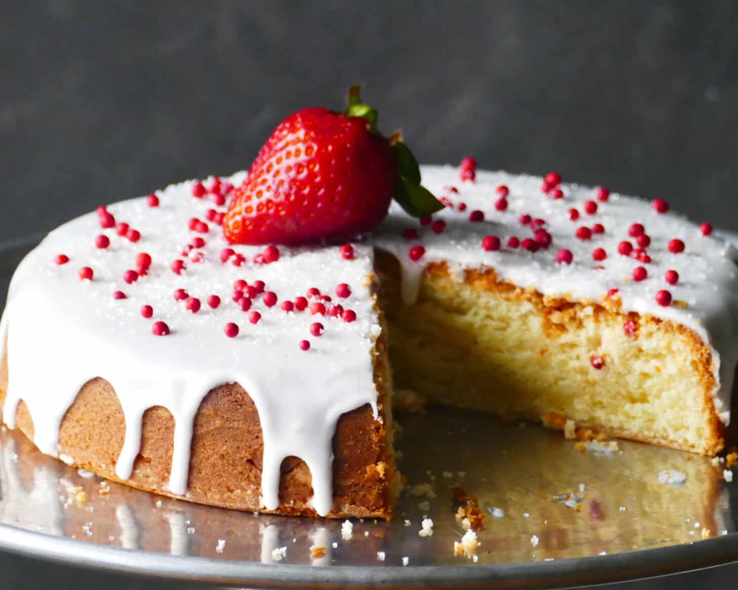 Frosted air fryer pound cake with a strawberry on top on metal tray.