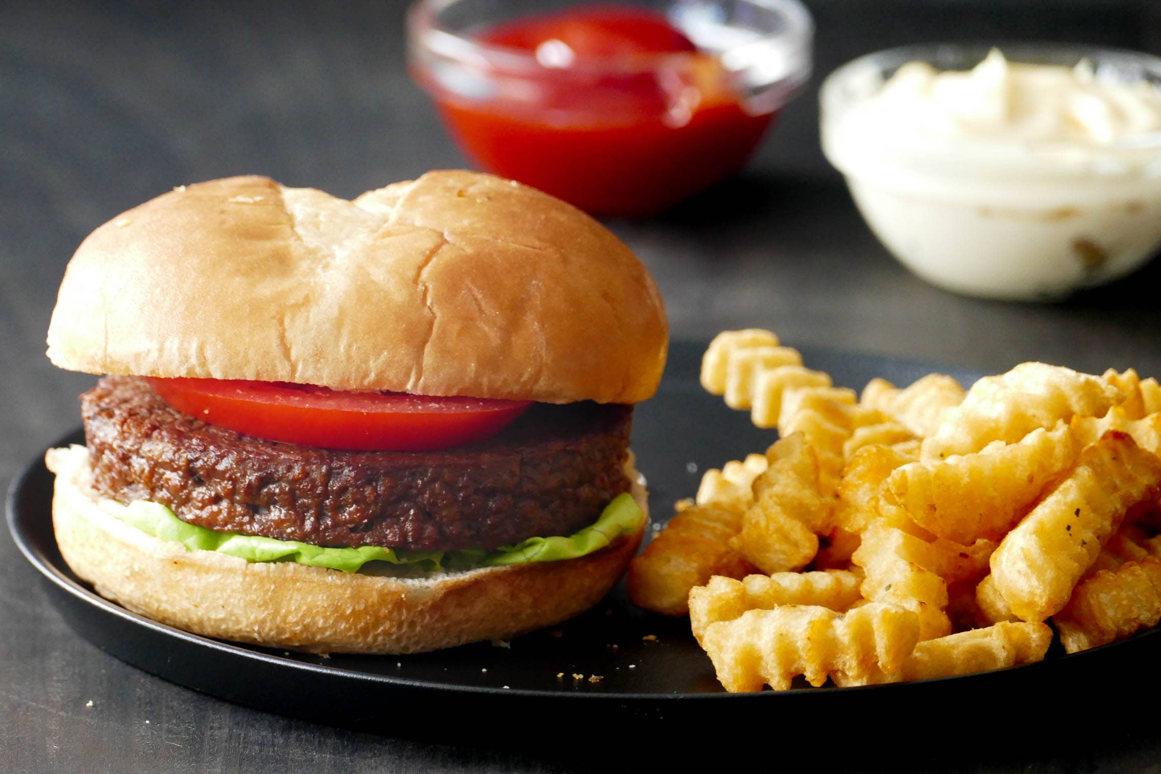 Air Fryer Frozen Impossible Burger on bun with lettuce, cheese, and tomato and fries on a plate.