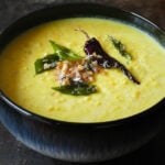 Bowl of Kerala parippu curry with fried curry leaves, onions, and chili.