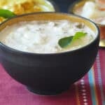 Cucumber kichadi in brown bowl with curry leaf on top.