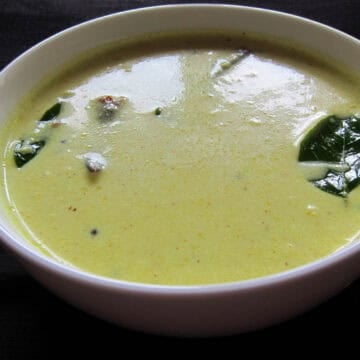 Moru curry with dried chilis and curry leaves in a white bowl.